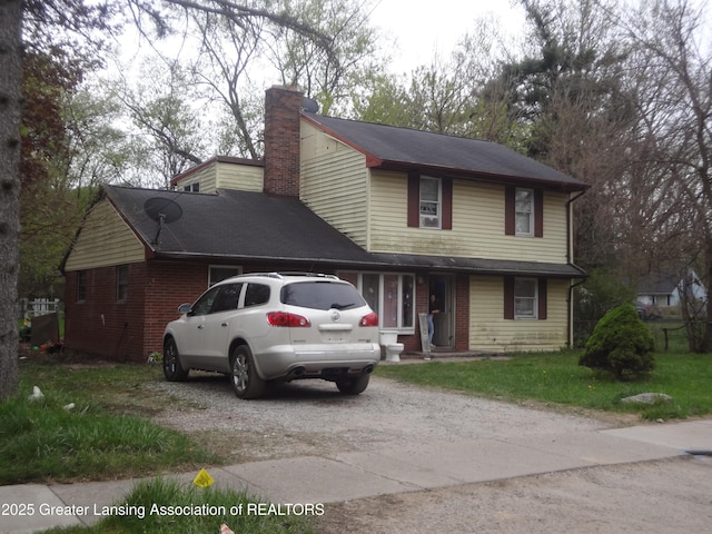 traditional home featuring driveway, a chimney, and a front yard