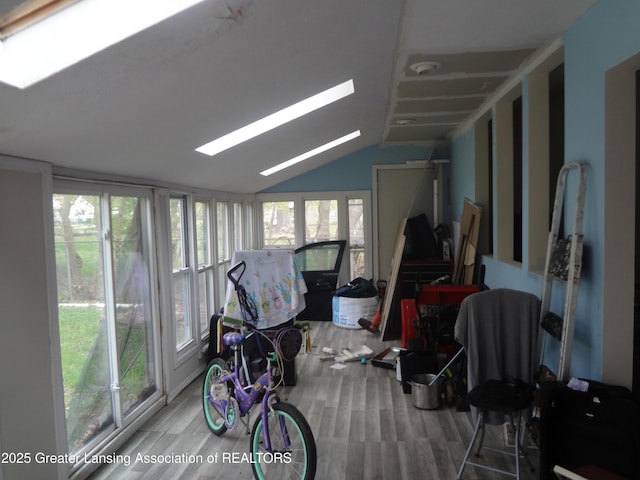 sunroom / solarium featuring wood finished floors, vaulted ceiling with skylight, and a wealth of natural light