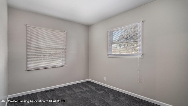 empty room featuring baseboards and dark carpet
