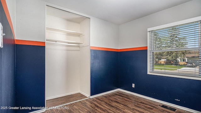 empty room featuring baseboards, wood finished floors, and visible vents