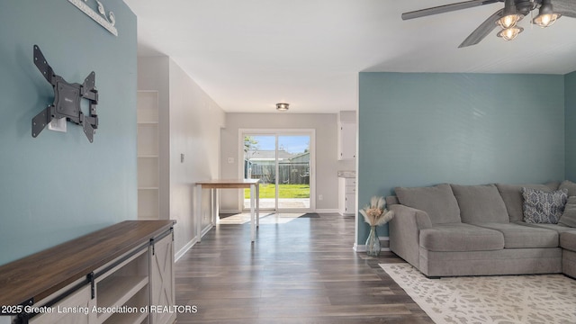 living area featuring a ceiling fan, baseboards, and dark wood finished floors