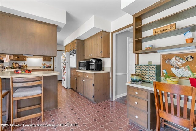 12188 Forest Meadow Dr, Perry, MI 48872 - kitchen featuring open shelves, a kitchen breakfast bar, light countertops, stainless steel microwave, and brown cabinets