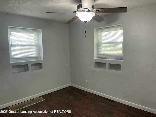spare room featuring baseboards, a wealth of natural light, dark wood-style flooring, and visible vents