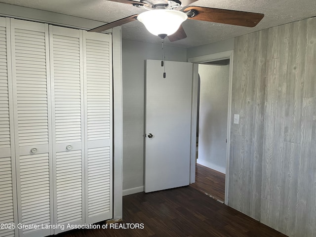 unfurnished bedroom with a closet, dark wood-style flooring, baseboards, ceiling fan, and a textured ceiling