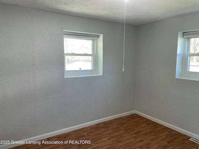 empty room with baseboards, visible vents, a textured ceiling, and dark wood-type flooring
