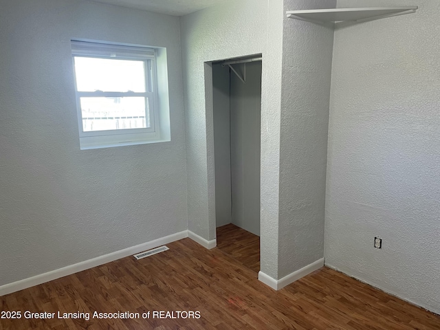 unfurnished bedroom with baseboards, a textured wall, wood finished floors, and visible vents
