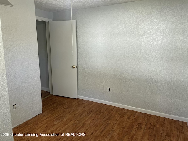 empty room with a textured ceiling, baseboards, a textured wall, and wood finished floors