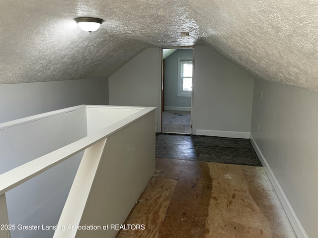 additional living space featuring baseboards, a textured ceiling, and vaulted ceiling