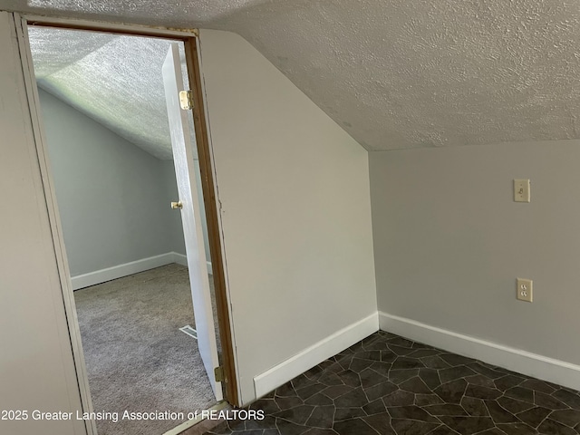 additional living space featuring a textured ceiling, vaulted ceiling, and baseboards