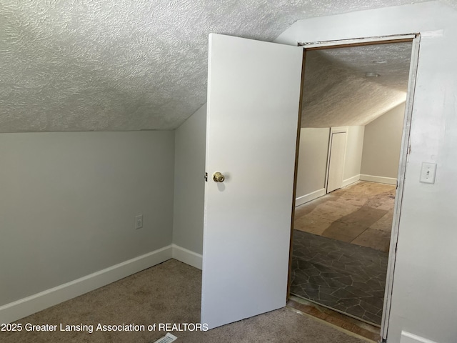 additional living space with baseboards, vaulted ceiling, and a textured ceiling
