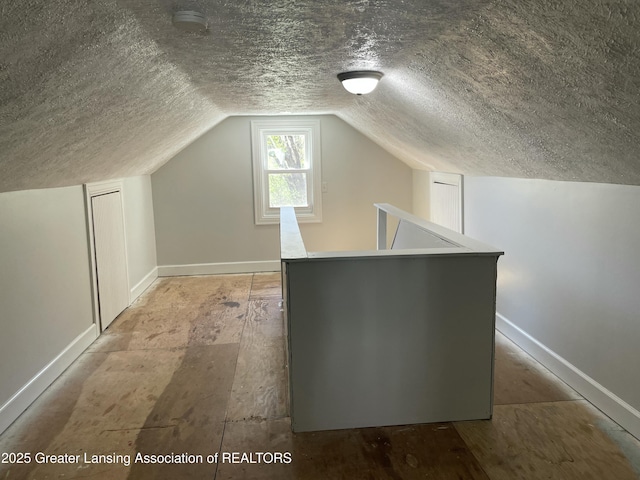 additional living space with a textured ceiling, vaulted ceiling, and baseboards
