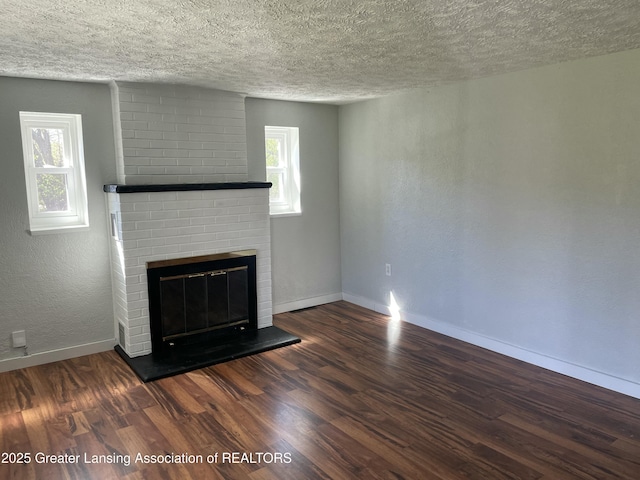 unfurnished living room with baseboards, a brick fireplace, a textured ceiling, and wood finished floors