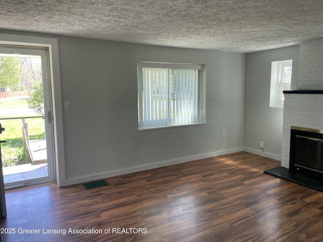 unfurnished living room with visible vents, wood finished floors, a fireplace, baseboards, and a textured ceiling