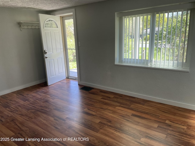 foyer with baseboards, visible vents, and dark wood-type flooring