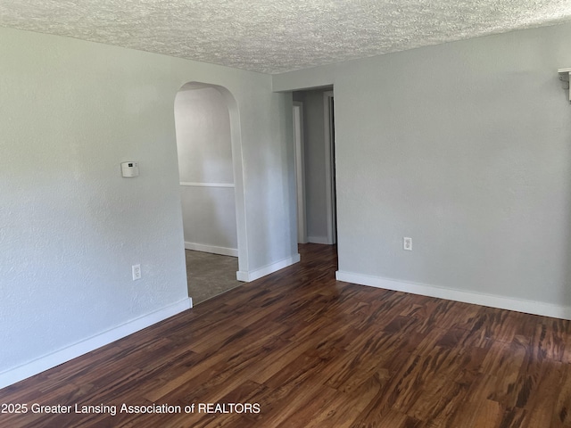 spare room featuring arched walkways, a textured ceiling, and dark wood-type flooring