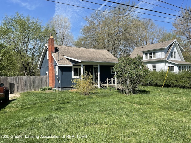view of front of property with a shingled roof, a front lawn, fence, and a chimney