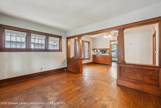 spare room featuring wood-type flooring, ornate columns, baseboards, and a textured ceiling