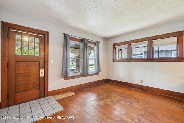 foyer featuring baseboards, a textured ceiling, a wealth of natural light, and wood finished floors