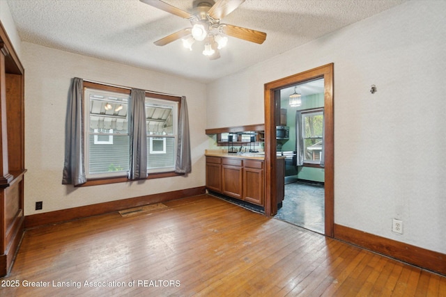 interior space featuring a textured ceiling, baseboards, a ceiling fan, and light wood-style flooring