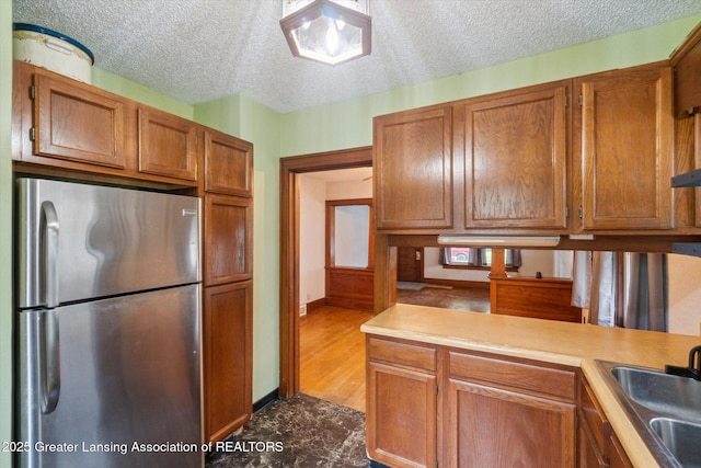 kitchen featuring brown cabinetry, freestanding refrigerator, a sink, and light countertops
