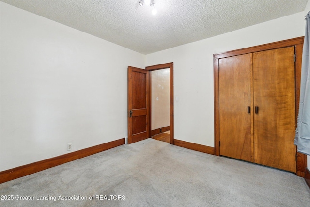 unfurnished bedroom with baseboards, a closet, a textured ceiling, and light colored carpet