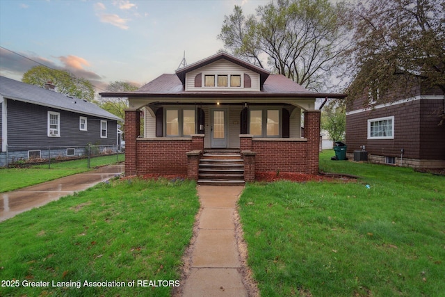 bungalow-style house featuring fence, a front yard, brick siding, a porch, and central air condition unit