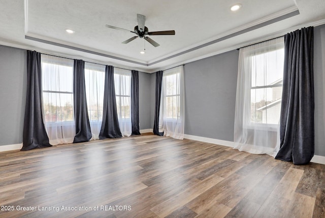 empty room featuring baseboards, ornamental molding, a tray ceiling, and wood finished floors