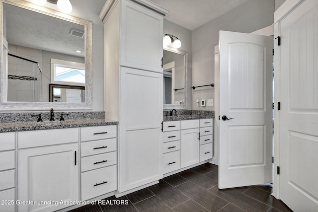 full bath featuring visible vents, two vanities, a sink, and a stall shower