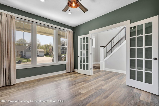 unfurnished room featuring ceiling fan, french doors, wood finished floors, stairway, and baseboards