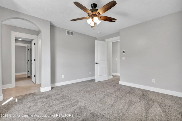 unfurnished bedroom featuring carpet floors, baseboards, arched walkways, and visible vents