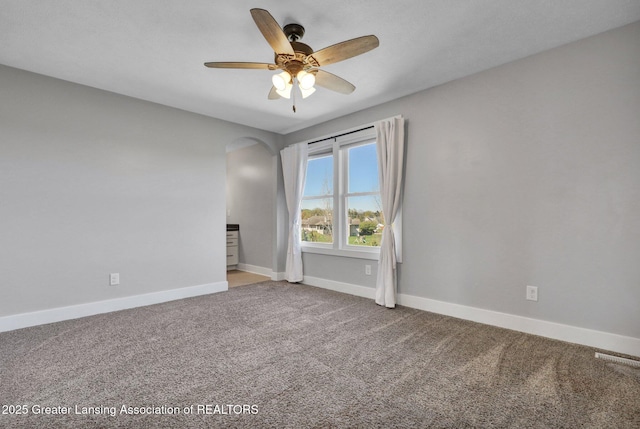 carpeted empty room featuring baseboards, ceiling fan, arched walkways, and visible vents