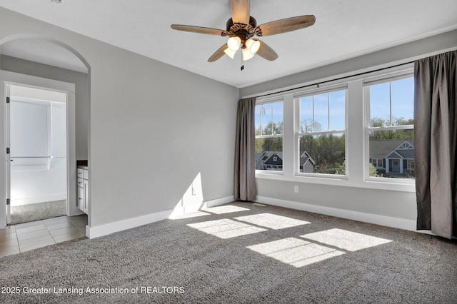 spare room featuring baseboards, a ceiling fan, carpet, and arched walkways