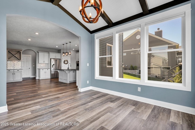 unfurnished living room featuring dark wood-style flooring, a sink, lofted ceiling with beams, arched walkways, and a notable chandelier