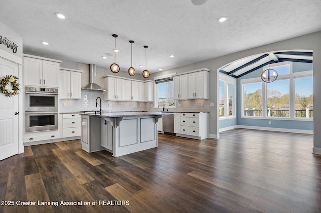 kitchen featuring double oven, wall chimney exhaust hood, plenty of natural light, and backsplash