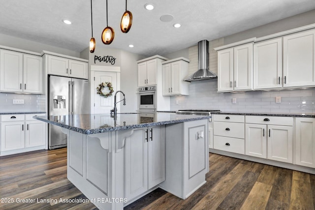 kitchen with wall chimney range hood, tasteful backsplash, a sink, high end refrigerator, and dark stone counters