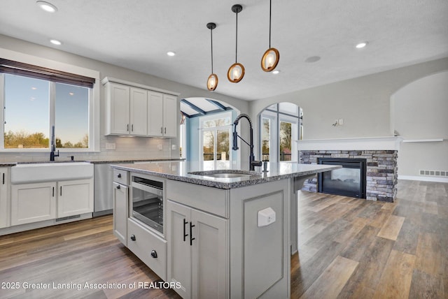 kitchen with a sink, arched walkways, stone counters, and stainless steel appliances