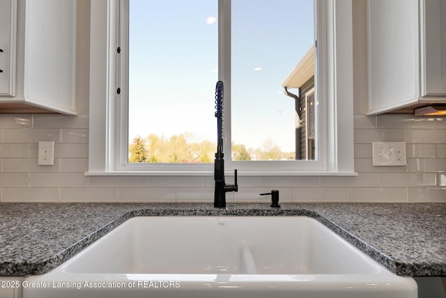 interior details featuring a sink, white cabinetry, dark stone counters, and tasteful backsplash