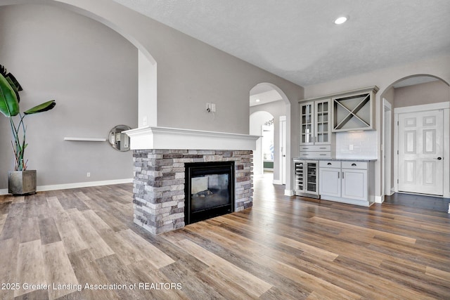 unfurnished living room featuring a stone fireplace, baseboards, wood finished floors, lofted ceiling, and wine cooler