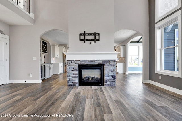 unfurnished living room with baseboards, dark wood finished floors, a high ceiling, and beverage cooler
