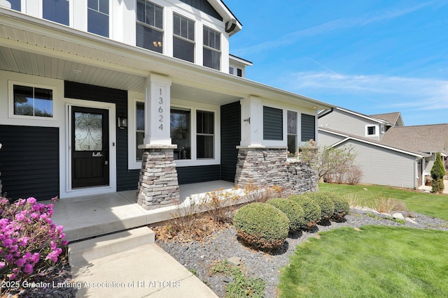 entrance to property featuring a porch, a yard, and stone siding