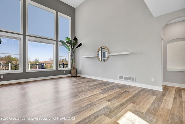 interior space featuring visible vents, arched walkways, wood finished floors, and vaulted ceiling