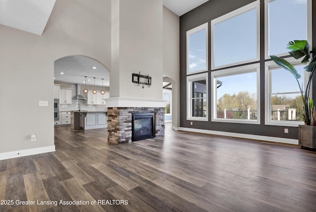 unfurnished living room with arched walkways, baseboards, dark wood-type flooring, and a towering ceiling