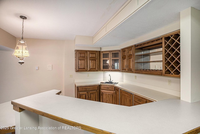 3796 Viceroy Dr, Okemos, MI 48864 - kitchen with brown cabinets, light countertops, decorative light fixtures, a sink, and glass insert cabinets