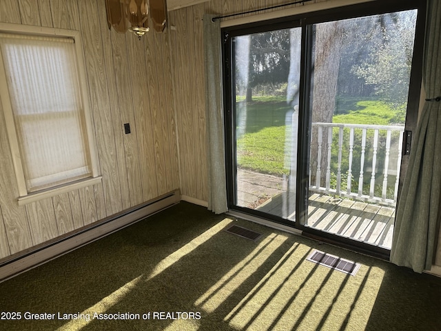 unfurnished dining area with carpet, baseboard heating, wood walls, and a healthy amount of sunlight
