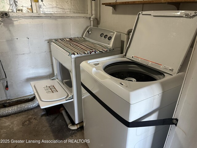 washroom with concrete block wall, laundry area, and washing machine and dryer