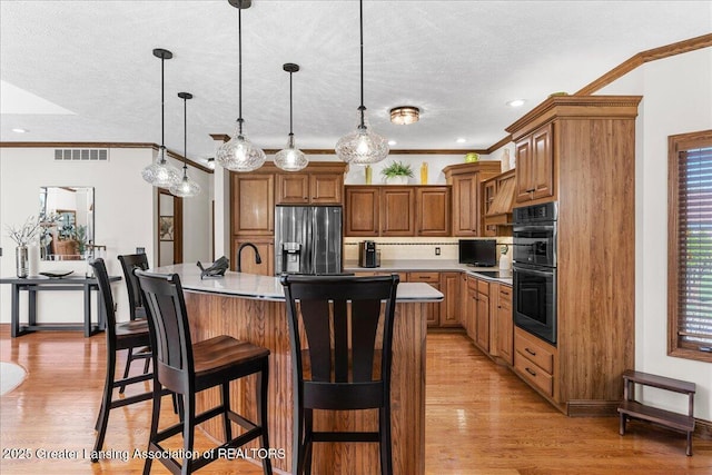 3012 Appaloosa Way, Lansing, MI 48906 - kitchen featuring stainless steel fridge, double oven, brown cabinetry, visible vents, and a center island with sink