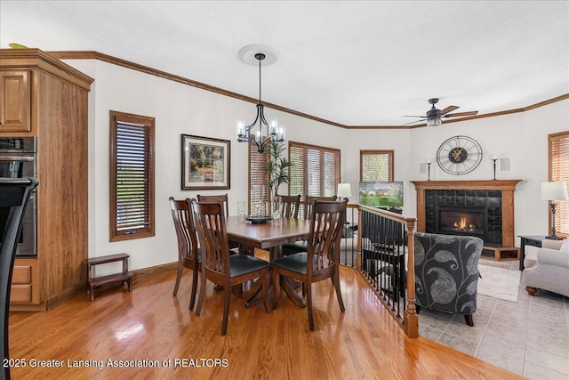 3012 Appaloosa Way, Lansing, MI 48906 - dining room with crown molding, baseboards, a tiled fireplace, light wood-style flooring, and ceiling fan with notable chandelier