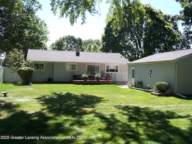 rear view of house featuring a yard, fence, a wooden deck, and a chimney