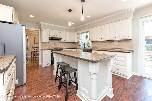 kitchen featuring under cabinet range hood, stainless steel appliances, dark wood-style floors, backsplash, and ornamental molding