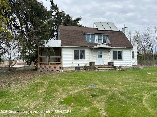 rear view of house featuring a yard, a shingled roof, a chimney, and roof mounted solar panels